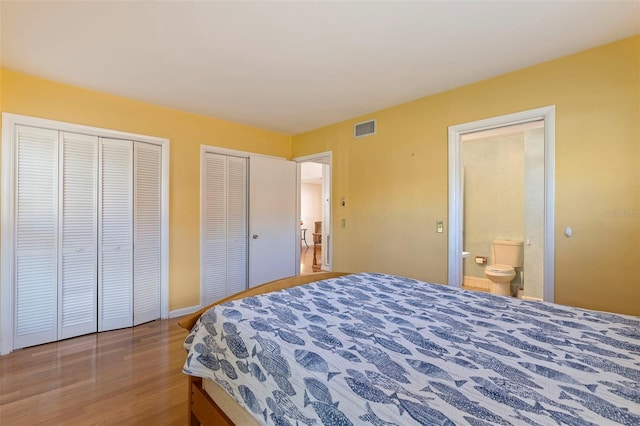 bedroom featuring connected bathroom, wood-type flooring, and two closets