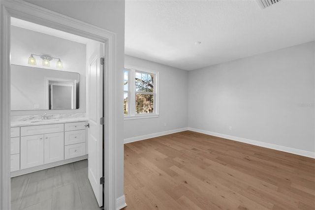 interior space with a textured ceiling, light hardwood / wood-style floors, sink, and ensuite bath