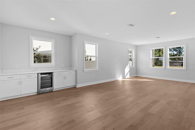 bar with light hardwood / wood-style floors, white cabinetry, beverage cooler, and a healthy amount of sunlight