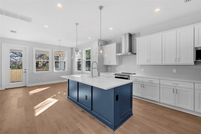 kitchen featuring a wealth of natural light, white cabinetry, a kitchen island with sink, and wall chimney range hood