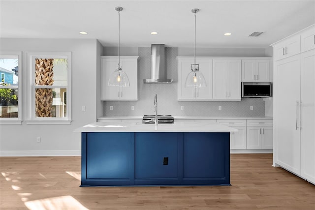 kitchen with appliances with stainless steel finishes, wall chimney range hood, pendant lighting, light hardwood / wood-style flooring, and white cabinets