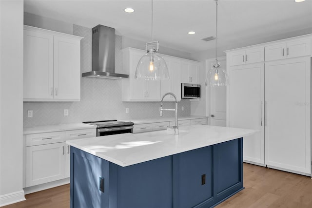 kitchen featuring white cabinets, light hardwood / wood-style flooring, wall chimney exhaust hood, appliances with stainless steel finishes, and decorative light fixtures