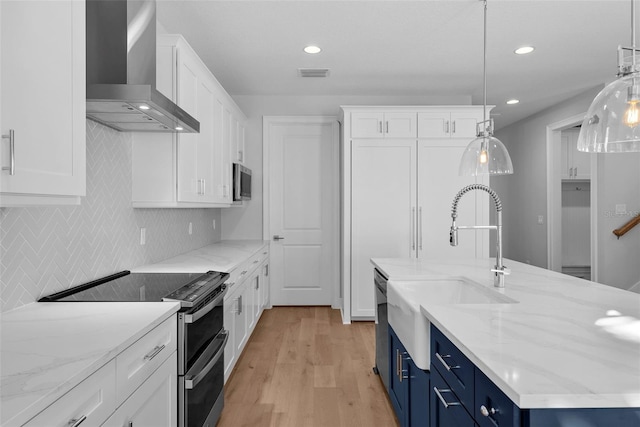 kitchen with wall chimney exhaust hood, stainless steel appliances, blue cabinets, pendant lighting, and white cabinets