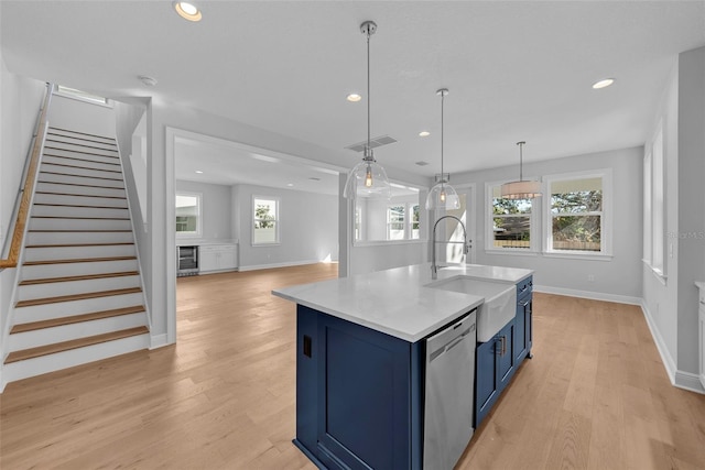 kitchen with a healthy amount of sunlight, an island with sink, stainless steel dishwasher, and blue cabinets