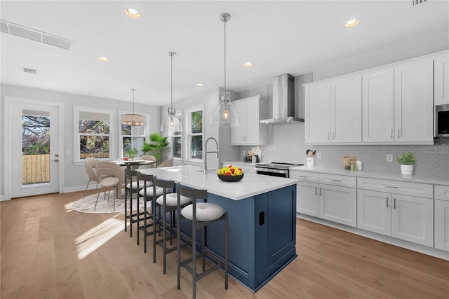 kitchen featuring white cabinetry, a kitchen island with sink, wall chimney exhaust hood, and appliances with stainless steel finishes