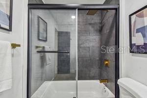 bathroom featuring bath / shower combo with glass door and toilet