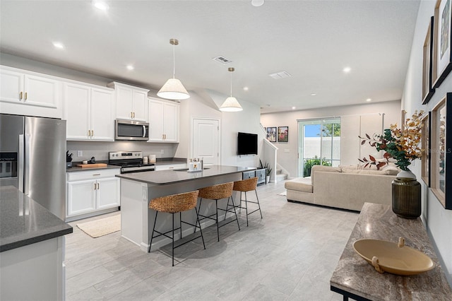 kitchen with white cabinetry, appliances with stainless steel finishes, decorative light fixtures, and a center island with sink