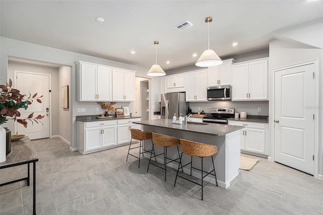 kitchen with pendant lighting, a center island with sink, white cabinets, and appliances with stainless steel finishes