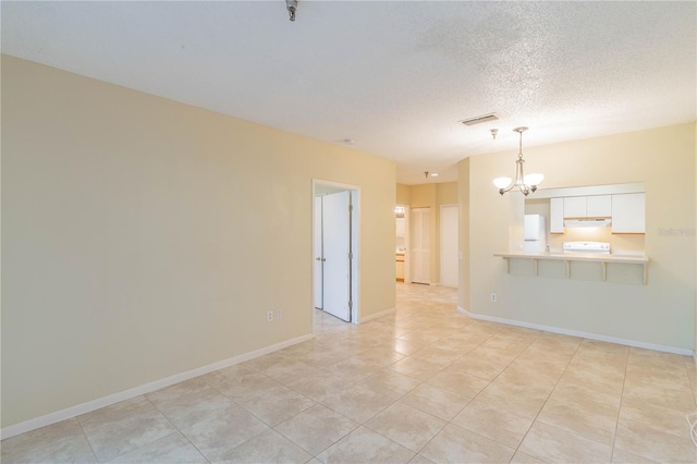 empty room featuring a notable chandelier, a textured ceiling, and light tile patterned flooring