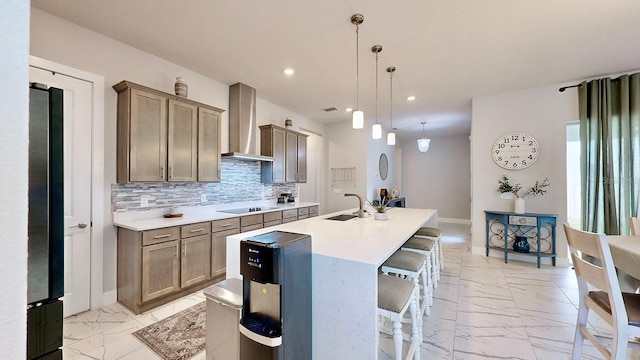 kitchen with sink, a kitchen breakfast bar, hanging light fixtures, a kitchen island with sink, and wall chimney exhaust hood