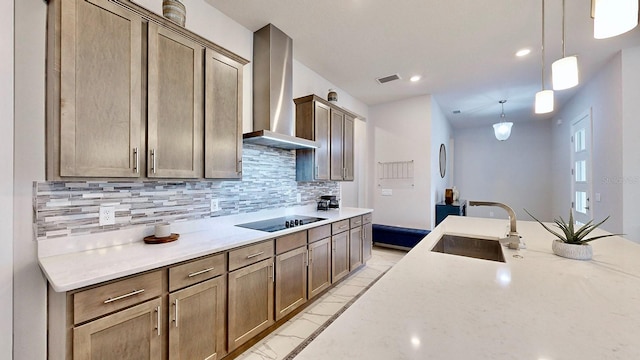 kitchen featuring sink, light stone counters, hanging light fixtures, black electric stovetop, and wall chimney range hood