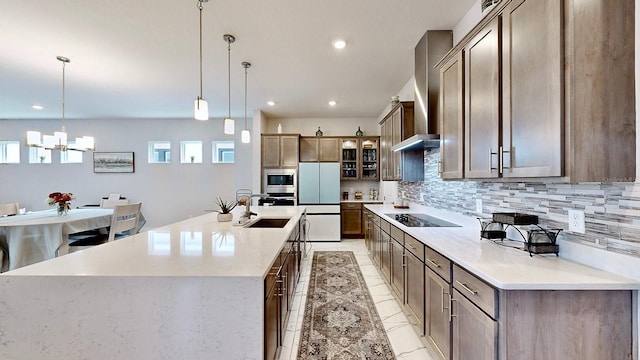 kitchen with appliances with stainless steel finishes, a large island, hanging light fixtures, and wall chimney range hood