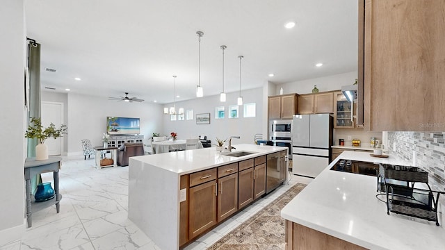 kitchen with pendant lighting, sink, appliances with stainless steel finishes, backsplash, and a center island with sink