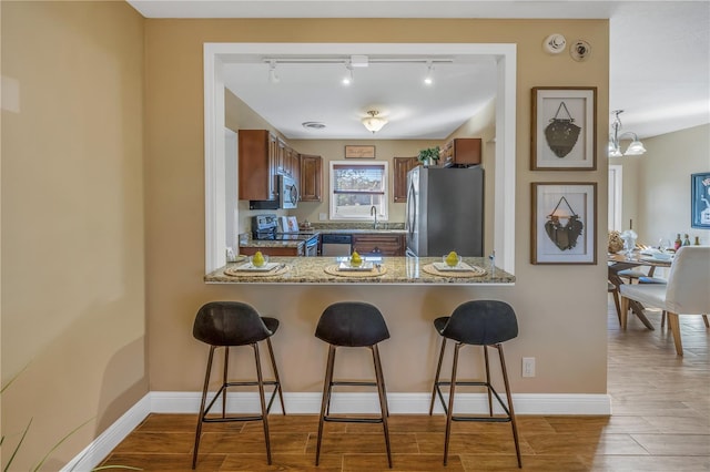 kitchen featuring stone counters, track lighting, light hardwood / wood-style flooring, appliances with stainless steel finishes, and a kitchen bar