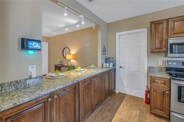 kitchen featuring light stone counters, rail lighting, light hardwood / wood-style floors, and appliances with stainless steel finishes