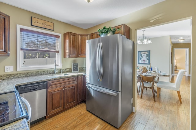 kitchen with appliances with stainless steel finishes, light stone counters, pendant lighting, a notable chandelier, and light hardwood / wood-style floors