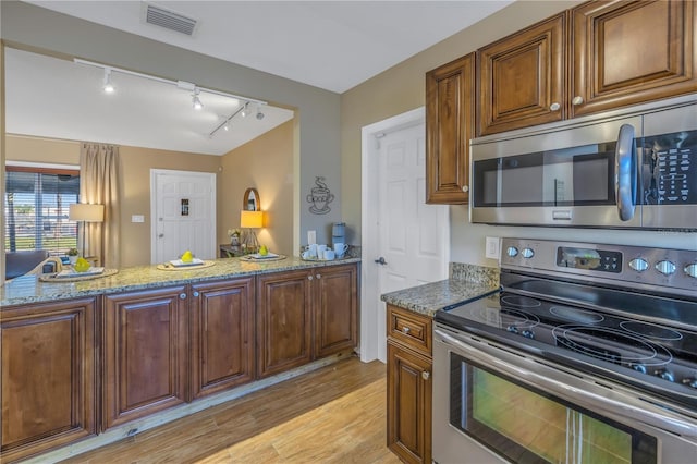 kitchen featuring rail lighting, stainless steel appliances, light stone counters, kitchen peninsula, and light hardwood / wood-style floors