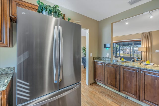 kitchen featuring light stone countertops, light wood-type flooring, rail lighting, and stainless steel refrigerator