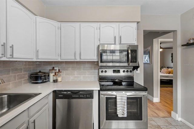 kitchen with white cabinets, backsplash, stainless steel appliances, and light hardwood / wood-style flooring