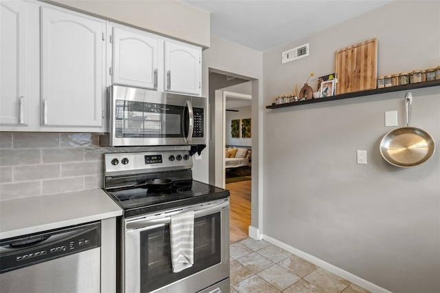 kitchen featuring decorative backsplash, appliances with stainless steel finishes, light tile patterned floors, and white cabinetry