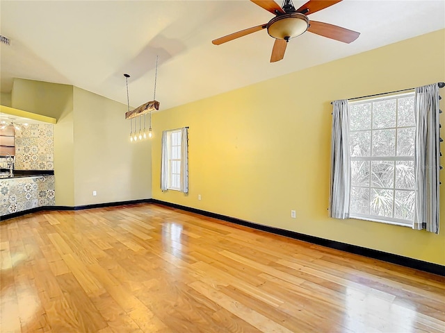 unfurnished living room featuring ceiling fan with notable chandelier, light wood-type flooring, and a healthy amount of sunlight