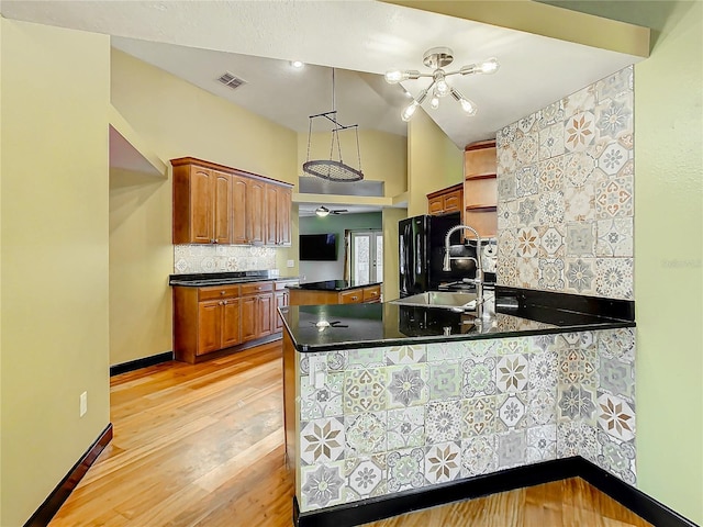 kitchen with black fridge, sink, light wood-type flooring, decorative light fixtures, and kitchen peninsula