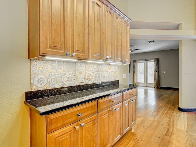 kitchen with ceiling fan, french doors, backsplash, dark stone countertops, and light wood-type flooring