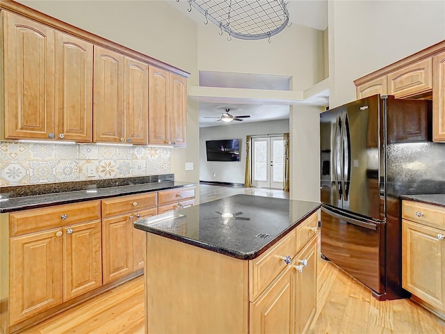 kitchen featuring ceiling fan, black refrigerator with ice dispenser, dark stone countertops, decorative backsplash, and light wood-type flooring