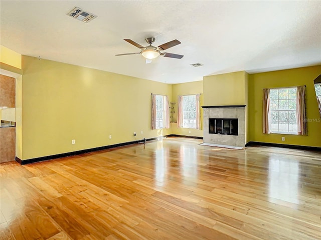 unfurnished living room featuring a tile fireplace, ceiling fan, and light wood-type flooring