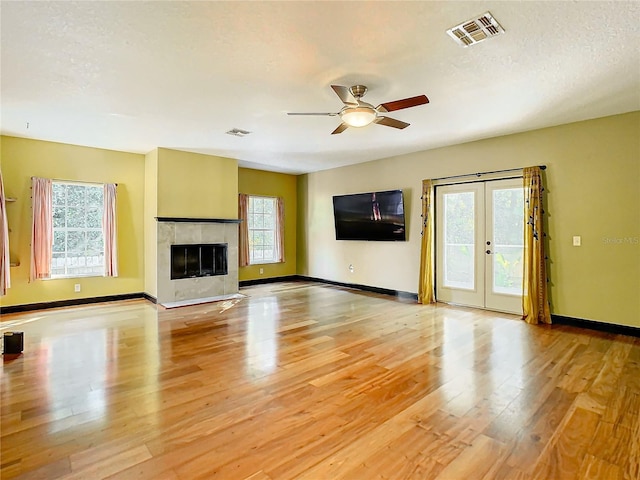 unfurnished living room with french doors, ceiling fan, light wood-type flooring, a textured ceiling, and a tiled fireplace