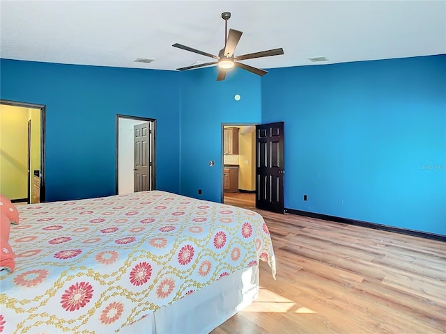 bedroom featuring ceiling fan, light wood-type flooring, ensuite bathroom, and vaulted ceiling