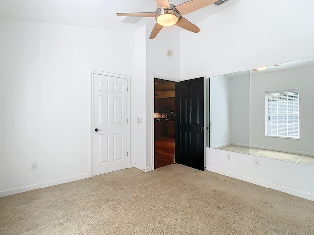 unfurnished bedroom with light carpet, ceiling fan, and a high ceiling