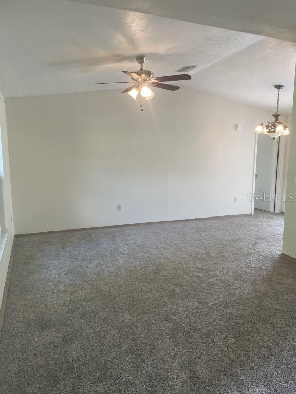 spare room featuring dark colored carpet, a textured ceiling, ceiling fan with notable chandelier, and vaulted ceiling