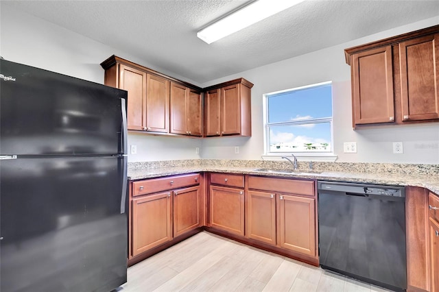 kitchen with sink, light stone counters, light hardwood / wood-style flooring, a textured ceiling, and black appliances