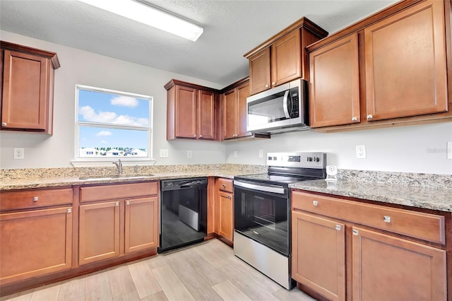 kitchen featuring light stone countertops, appliances with stainless steel finishes, a textured ceiling, sink, and light hardwood / wood-style floors