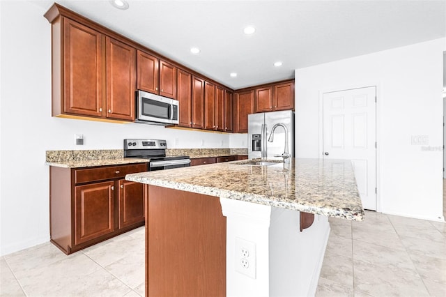 kitchen with a kitchen island with sink, stainless steel appliances, sink, and light stone counters