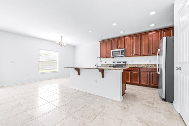 kitchen with stainless steel appliances, a chandelier, an island with sink, a breakfast bar, and light stone countertops