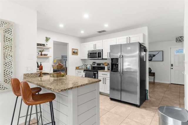 kitchen with kitchen peninsula, stainless steel appliances, white cabinetry, and light stone counters