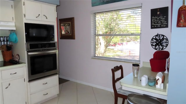 kitchen featuring stainless steel oven, white cabinetry, light tile patterned floors, and a wealth of natural light