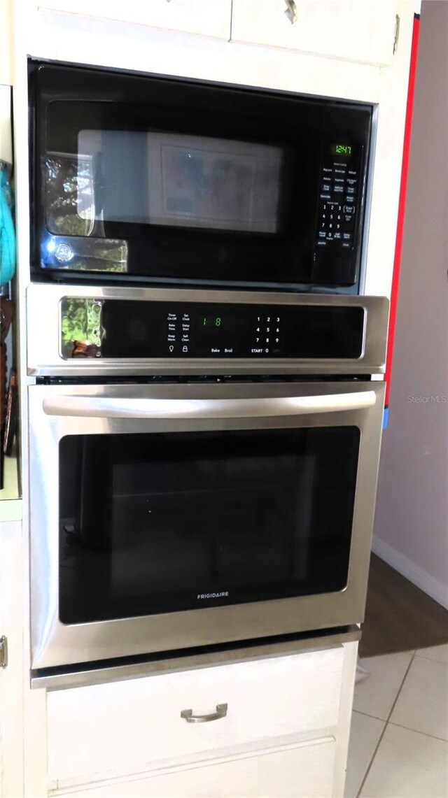 interior details with oven, tile patterned floors, white cabinetry, and black microwave