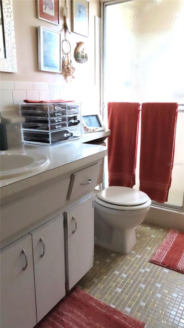 bathroom with vanity, toilet, a shower with shower door, and backsplash