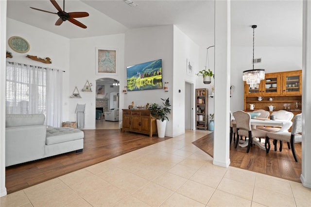 living room with high vaulted ceiling, a fireplace, ceiling fan with notable chandelier, and light tile patterned floors