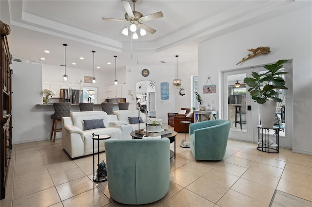 living room featuring a raised ceiling, light tile patterned floors, and ceiling fan