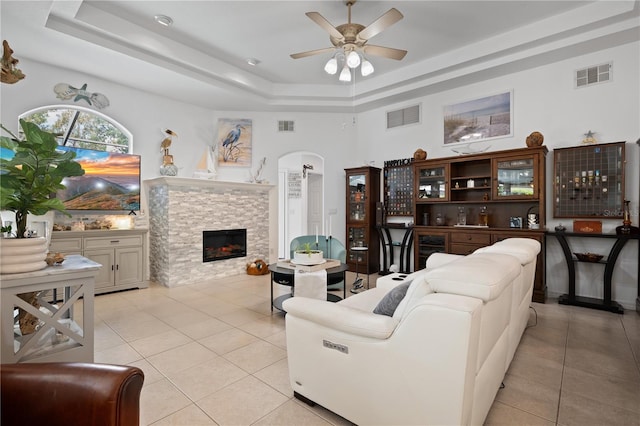 tiled living room with wine cooler, a stone fireplace, a raised ceiling, and ceiling fan