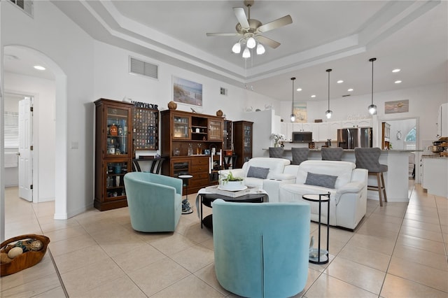 living room with a raised ceiling, ceiling fan, and light tile patterned flooring