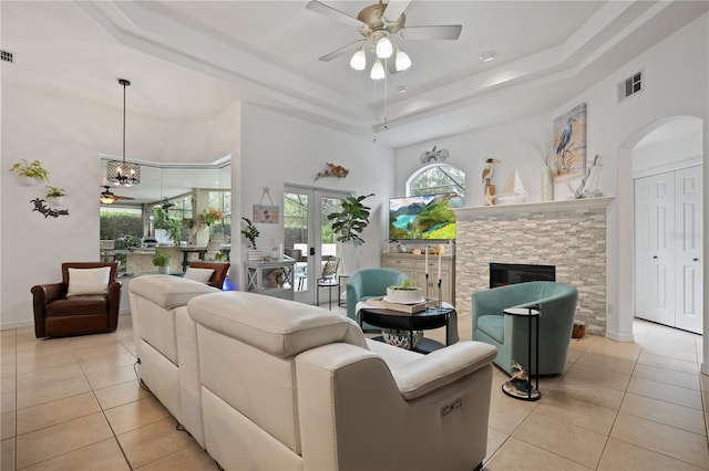 tiled living room with a tray ceiling, a fireplace, and ceiling fan