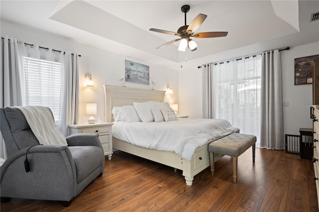 bedroom with dark hardwood / wood-style flooring, a tray ceiling, and ceiling fan