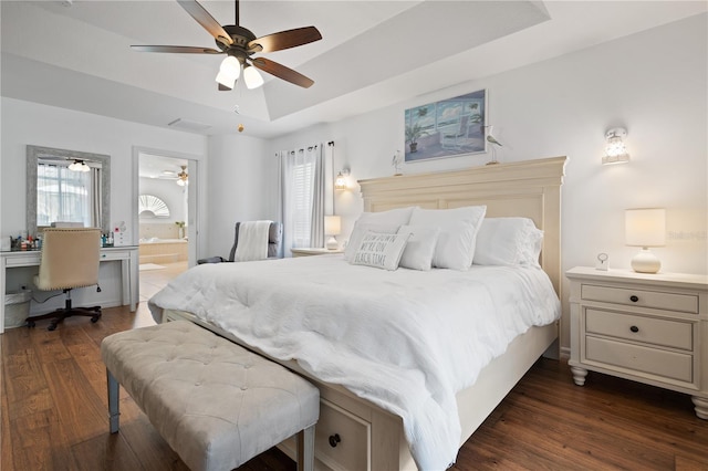 bedroom with dark wood-type flooring, connected bathroom, ceiling fan, and a tray ceiling