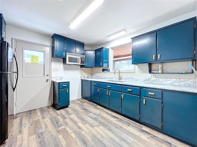 kitchen with blue cabinetry, black refrigerator, light wood-type flooring, and sink