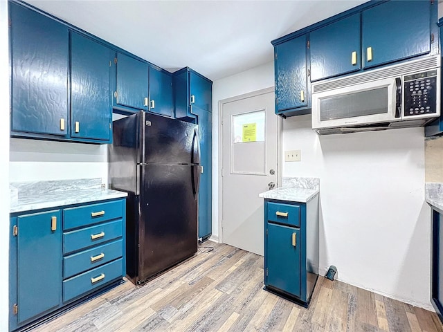 kitchen featuring black refrigerator, light wood-type flooring, and blue cabinetry